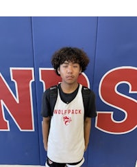 a young boy standing in front of a wall with a wolfpack logo