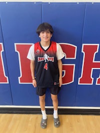 a boy in a basketball uniform standing in front of a wall