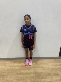 a young girl in a basketball uniform standing in a gym