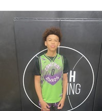 a young boy in a green and purple jersey standing in front of a wall