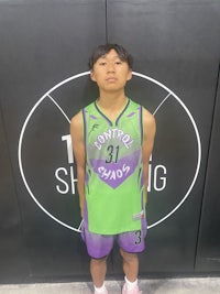 a young boy in a green and purple uniform standing in front of a basketball court