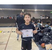 a young boy holding up a certificate in front of a basketball court