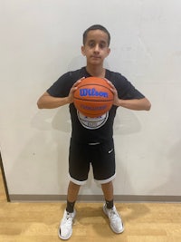 a young boy holding a basketball in front of a wall