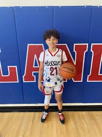 a young boy holding a basketball in front of a wall