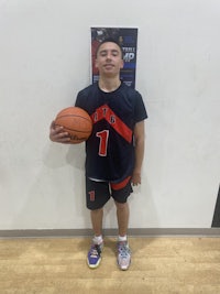a young man holding a basketball in front of a wall