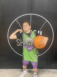 a young boy holding a basketball in front of a basketball court