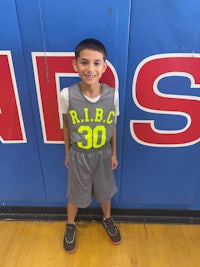 a young boy in a basketball uniform standing in front of a wall