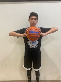 a young man holding a basketball in front of a wall