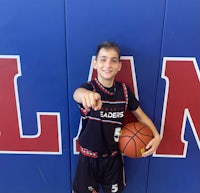 a young boy holding a basketball in front of a wall