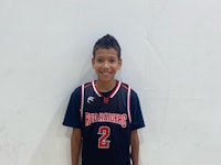 a young boy in a basketball uniform standing in front of a wall