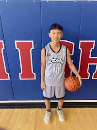 a young boy holding a basketball in front of a wall