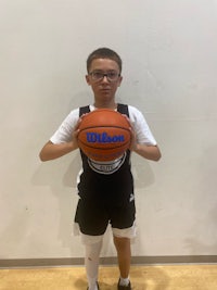 a young boy holding a basketball in front of a wall