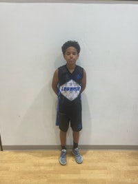 a young boy in a basketball uniform standing in front of a wall