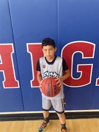 a young boy holding a basketball in front of a wall